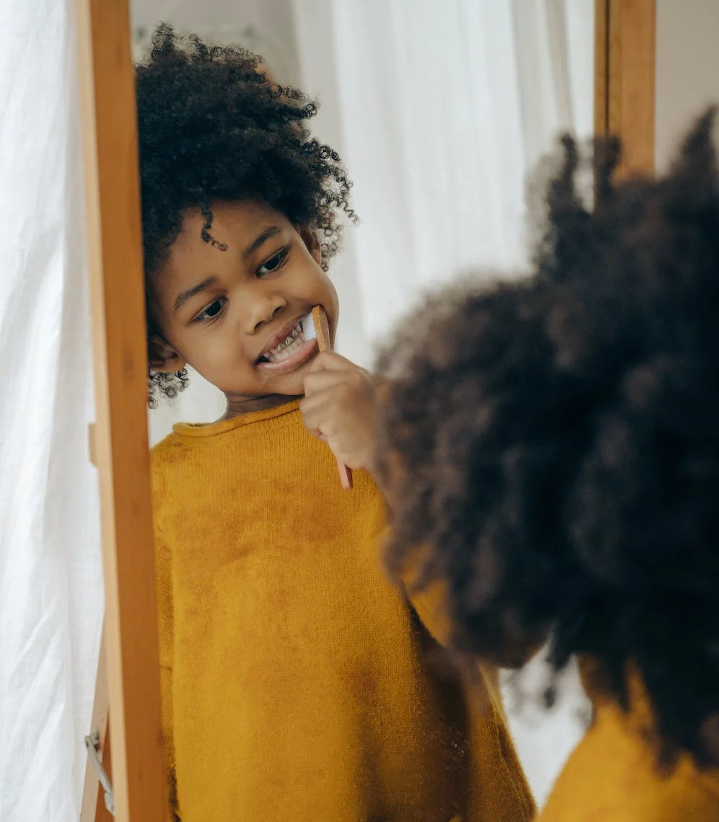 Child practicing self care for kids by brushing teeth